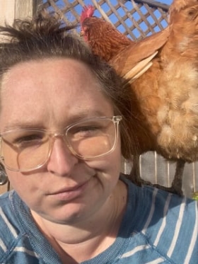 Justine with a chicken on her shoulder, she's pretending not to be super happy about it.